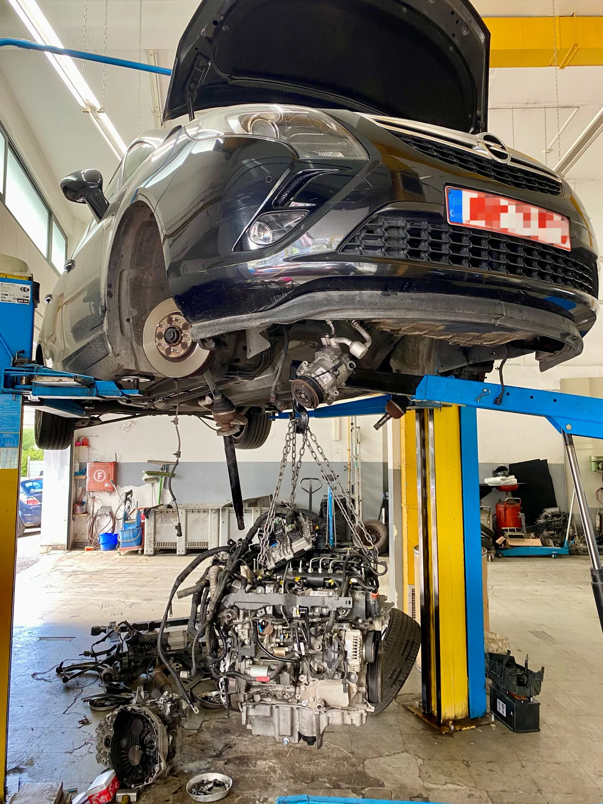 Car on a lift with a removed engine on the workshop floor